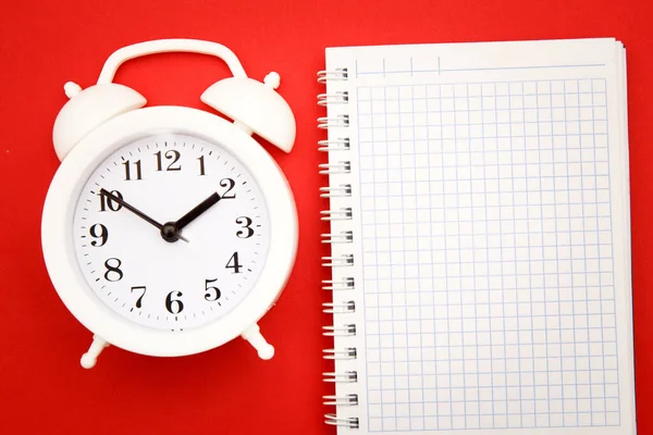 Reloj despertador blanco y cuaderno sobre fondo rojo, espacio vacío para texto —  Fotos de Stock