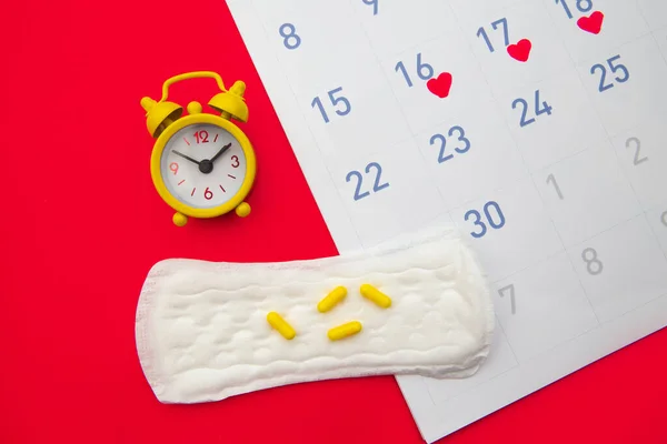 Menstruatiekalender met kussens, wekker, hormonale anticonceptiepillen op rode achtergrond. Vrouwelijke menstruatiecyclus concept. Pijnstillers voor menstruatiepijn — Stockfoto