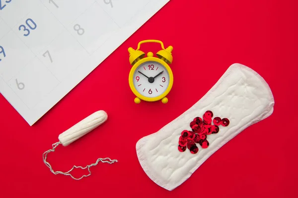 Menstruationskalender mit femininen Produkten und gelbem Wecker auf rotem Hintergrund — Stockfoto