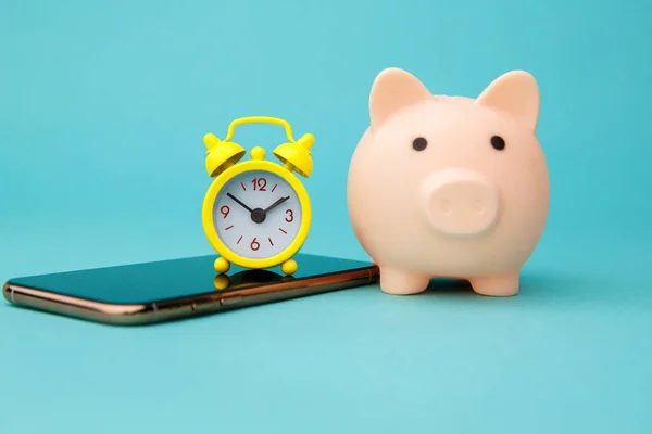 Smartphone, pink piggy bank and alarm clock isolated on blue background. Online shopping concept