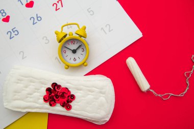 Kadınların adet döngüsü konsepti. Regl takvimi, pedleri, tamponları ve renkli arkaplanı olan alarm saati.