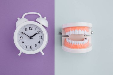 Renkli arka planda çalar saati olan beyaz kağıt diş. Diş sağlığı kavramına zaman