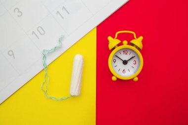 Calendar, cotton tampon and yellow alarm clock on colorful background. Females menstrual cycle concept clipart