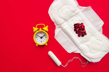 Kırmızı arkaplanda kırmızı parıltılı ve sarı alarm saati olan adet pedi. Adet dönemi konsepti. Regl gecikmesi konsepti