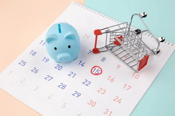 Seizoensgebonden kortingen. Piggy bank met kalender, supermarkt trolley op een kleurrijke achtergrond — Stockfoto