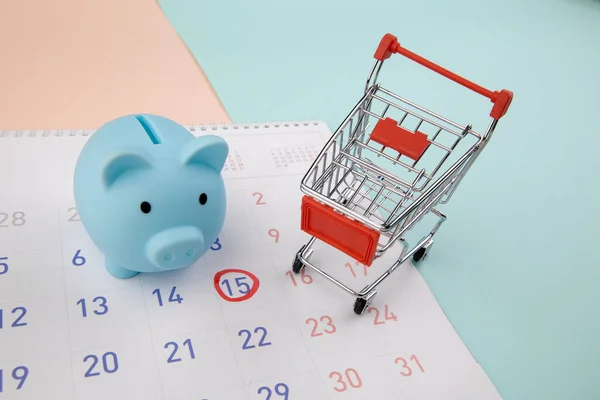 Venda sazonal. Piggy bank com calendário, carrinho de supermercado em um fundo colorido — Fotografia de Stock