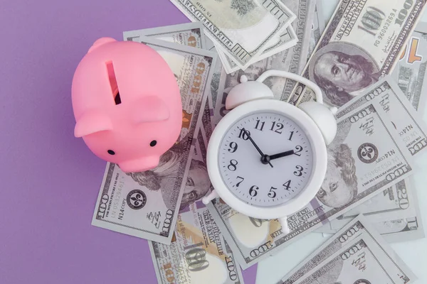Alarm clock on dollars banknotes and piggy bank on colorful background. Time to invest