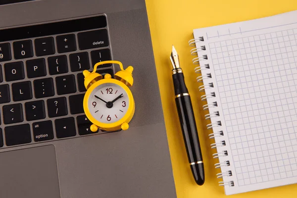 Концепция рабочего места домашнего офиса. Ноутбук, часы, ноутбук и ручка на желтом фоне — стоковое фото