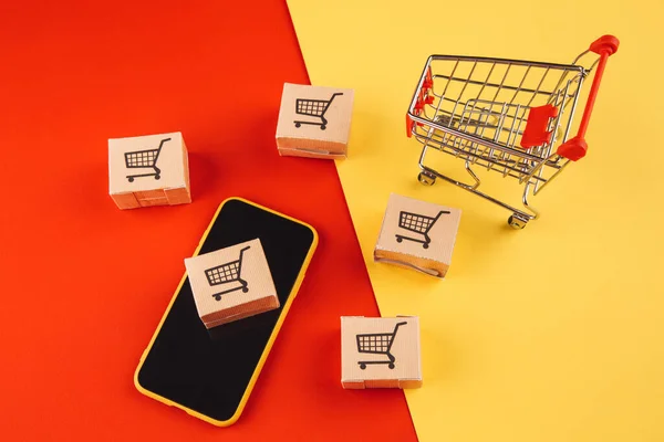 Concepto de compras online. Cajas en smartphone y carrito aislado sobre fondo colorido — Foto de Stock