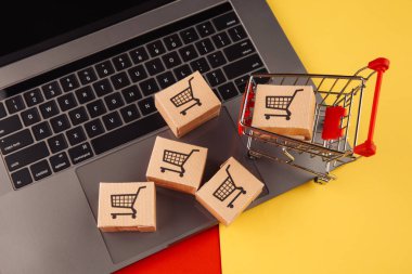 İnternetten alışveriş konsepti. Dizüstü bilgisayardaki kutular ve renkli arkaplanda izole edilmiş alışveriş arabaları