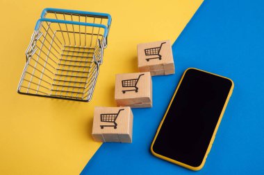 İnternetten alışveriş konsepti. Küçük kutuları ve mavi sarı arka planda alışveriş sepeti olan akıllı telefon.