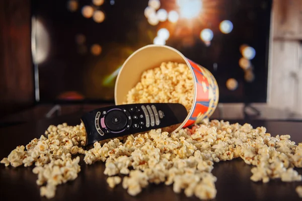 Craft bowl of popcorn on the dark table and TV remote control with TV set. — Stok Foto