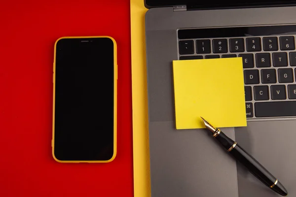 Concetto di scrivania per ufficio. Laptop, smartphone e penna con nota adesiva gialla su sfondo rosso. Vista dall'alto — Foto Stock