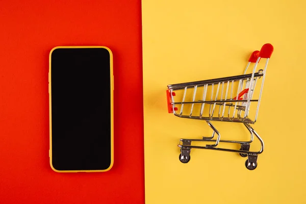 Online shopping concepts with mockup trolley and smartphone on yellow red background. Ecommerce market. Transportation logistic. Business retail