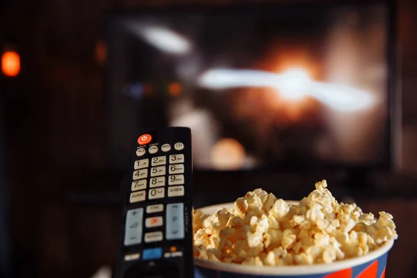 Tazón artesanal de palomitas de maíz en la mesa oscura y TV control remoto con televisor . — Foto de Stock