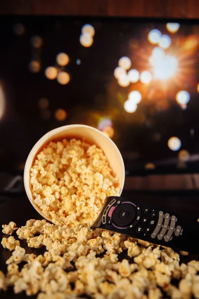 Craft bowl of popcorn on the dark table and TV remote control with TV set. — Stok Foto