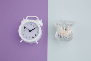 Renkli arka planda çalar saati olan diş. Diş sağlığı kavramına zaman
