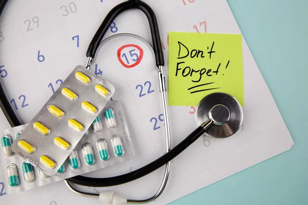 Visit The Doctor Reminder on sticky note, pills and stethoscope on a calendar