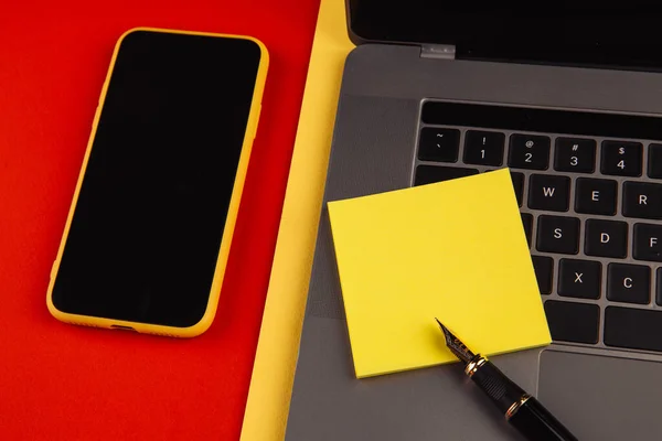 Concetto di scrivania per ufficio. Laptop, smartphone e penna con nota adesiva gialla su sfondo rosso — Foto Stock