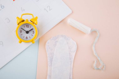 Takvim, pamuklu tampon ve pembe arka planda sarı alarm saati. Dişilerin adet döngüsü kavramı