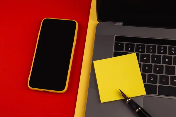 Концепция рабочего места домашнего офиса. Ноутбук, смартфон и липкая нота на красном фоне — стоковое фото