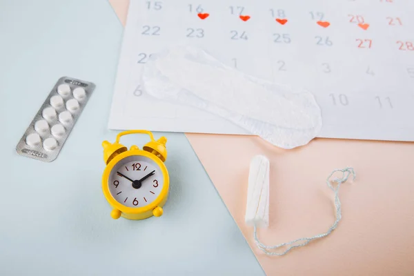 Календарь, тампон и желтый будильник на сине-розовом фоне. Концепция менструального цикла у женщин — стоковое фото