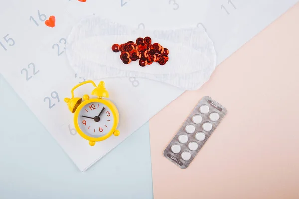 Менструальный календарь с колодками, будильником и противозачаточными таблетками. Концепция менструационного периода. Средство от боли при менструации — стоковое фото