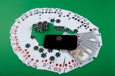 Akıllı telefon ve poker fişleri ile yeşil bir masanın üzerinde oyun kartları ve para banknotları. Online kumarhane konsepti