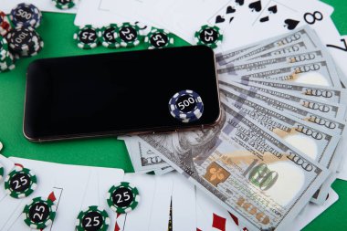 Çevrimiçi kumarhane konsepti, iskambil kartları, para, zar çipleri ve yeşil masada telif alanı olan akıllı telefon.