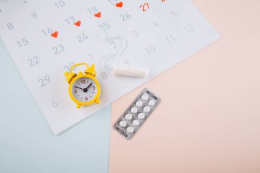 Sarı alarmlı regl takvimi, pamuklu tampon ve pembe arka planda doğum kontrol hapları. Kadın kritik günler, kadın hijyen koruma konsepti