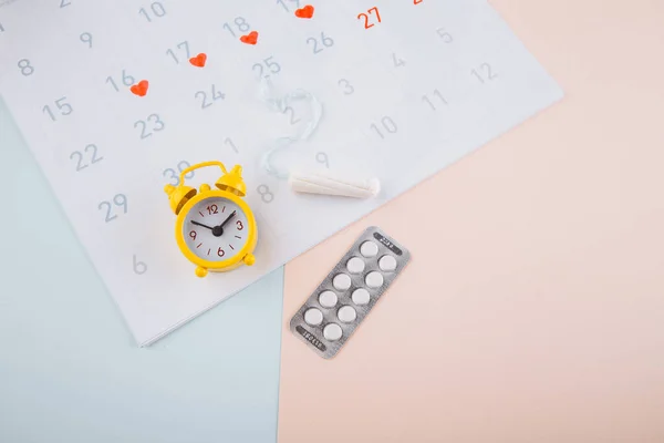 Menstruation calendar with yellow alarm, cotton tampon and contraceptive pills on pink background. Woman critical days, woman hygiene protection concept
