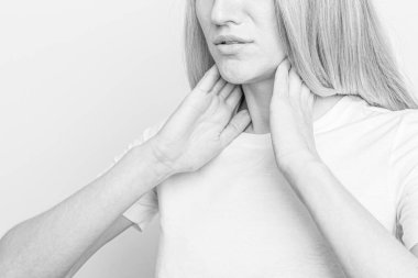 Tiroid bezini tek başına kontrol eden bir kadın. Beyaz tişörtlü bir kadının kırmızı noktalı boynuna dokunuşunu yakından çek. Tiroid bozukluğu guatr, hipertiroid, hipotiroid, tümör ya da kanseri içerir. Sağlık hizmetleri.