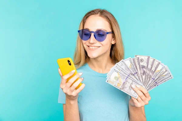 Młoda dama odizolowana na niebieskim tle. Kamera widoczna na wyświetlaczu telefonu komórkowego z pieniędzmi. — Zdjęcie stockowe