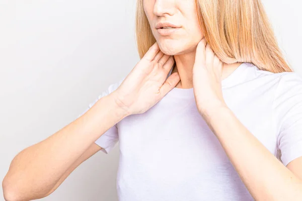 Weibchen checken Schilddrüse selbst. Großaufnahme einer Frau in weißem T-Shirt, die den Hals mit rotem Fleck berührt. Schilddrüsenerkrankungen umfassen Kropf, Schilddrüsenüberfunktion, Schilddrüsenunterfunktion, Tumor oder Krebs. Gesundheitsversorgung. — Stockfoto