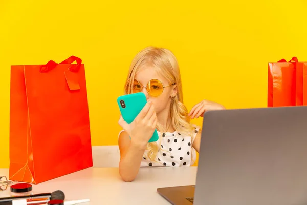 Klein meisje blogger met blauwe telefoon maken van video voor blog en volgers zitten in de gele studio geïsoleerd. — Stockfoto