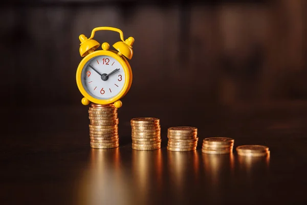 Le temps est un concept d'argent. Un réveil et une pile de pièces sur une table en bois — Photo