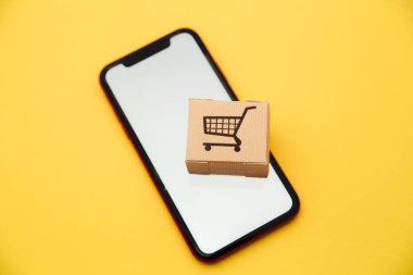 İnternet konsepti üzerinden çevrimiçi alışveriş ve ekommerce: sarı zemin üzerinde kutu ve akıllı telefon