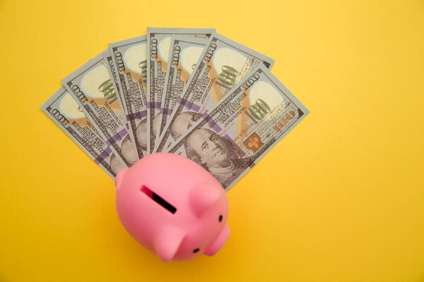 Свиная копилка со стодолларовыми купюрами на желтом фоне. Семейный бюджет, сбережения