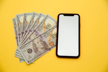 Sarı arka planda akıllı telefon ve dolar banknotları