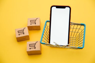 İnternet konsepti üzerinden çevrimiçi alışveriş ve ekommerce: sarı arka planda bir septte kutular ve akıllı telefon