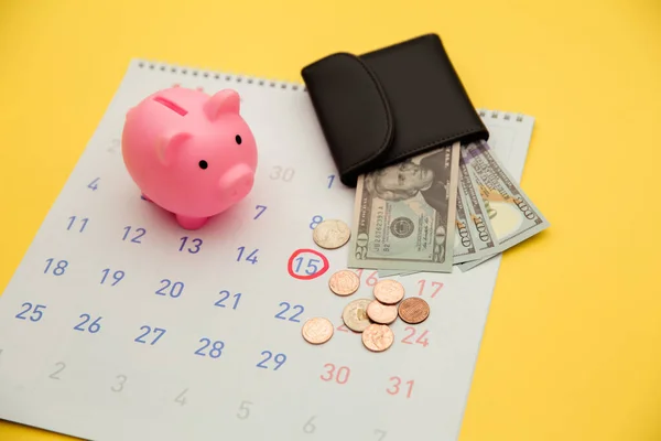 Yatırım yapma zamanı, iş konsepti. Pembe domuz kumbarası ve para banknotları ile cüzdan, sarı arka planda takvim — Stok fotoğraf