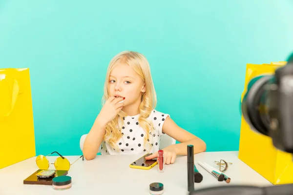 Gelukkig meisje zit aan het bureau in de blauwe studio te praten voor de camera voor vlog. Jonge schoonheid blogger opname video tutorial voor internet. — Stockfoto