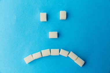 Mavi masadaki üzgün şeker surat. Tatlı yiyecekler dişlerine zararlıdır..