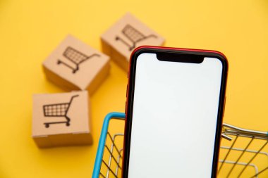 İnternet konsepti üzerinden çevrimiçi alışveriş ve ekommerce: sarı arka planda bir septte kutular ve akıllı telefon