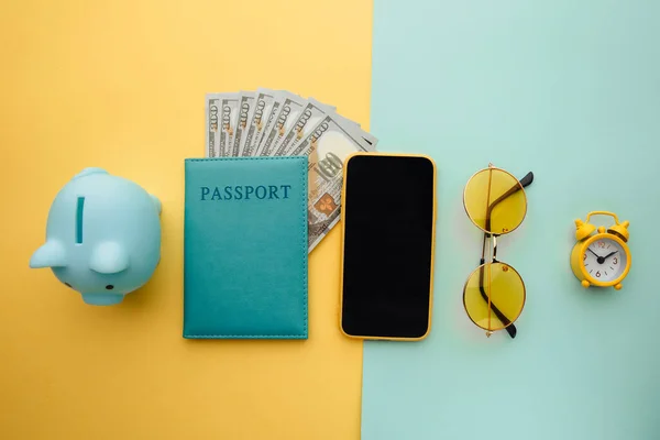 Save up for travelling. Travel planning with piggy bank, smartphone, sunglasses and passport with money on blue yellow background