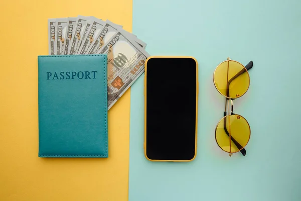 Planowanie podróży ze smartfonem, okularami przeciwsłonecznymi i paszportem z pieniędzmi na niebiesko żółtym tle — Zdjęcie stockowe