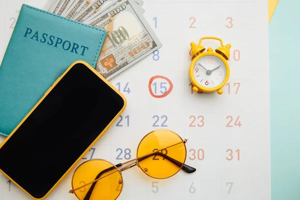 Calendario con pasaporte, gafas de sol y smartphone sobre fondo azul. Concepto de planificación vacacional —  Fotos de Stock