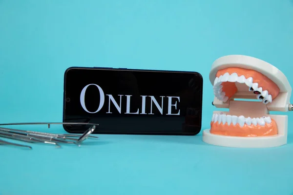Dentist online appointment. Phone with medical instruments and jaw isolated on the blue background.