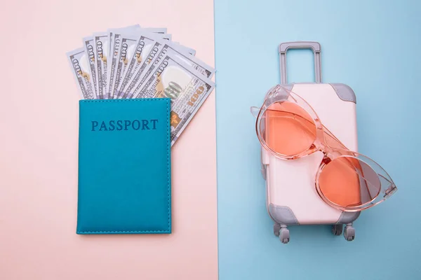 Maleta de viaje con gafas de sol y pasaporte con dinero sobre fondo rosa azulado. Concepto vacaciones de verano —  Fotos de Stock