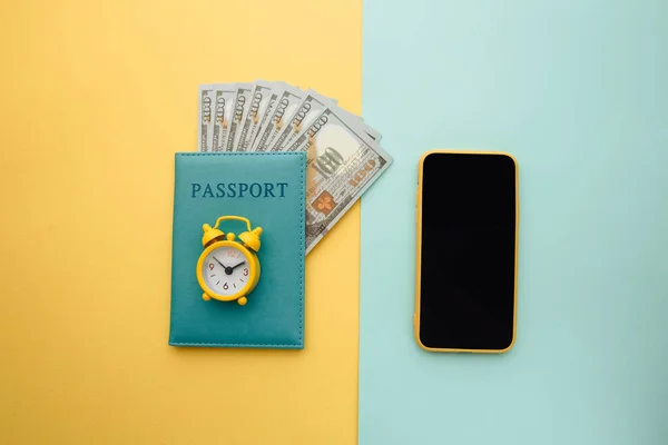 Planificación de viajes con smartphone, reloj despertador y pasaporte con dinero sobre fondo azul amarillo —  Fotos de Stock